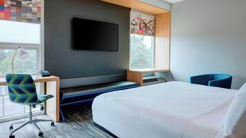 Un hotel moderno con una cama grande, un escritorio con silla, un televisor de pantalla plana en la pared y una ventana con vistas a árboles.
