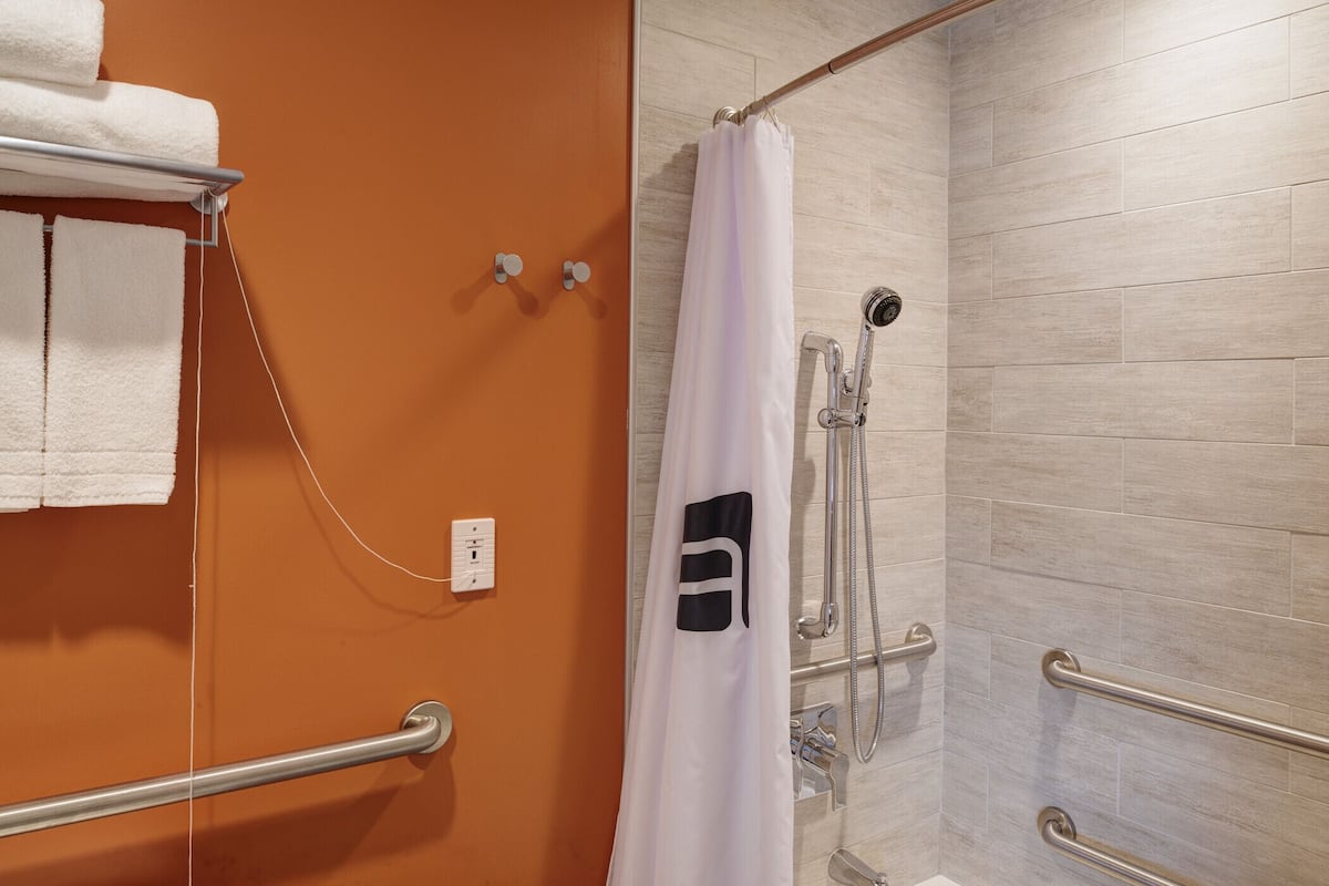 A bathroom with a shower, grab bars, and a towel rack.