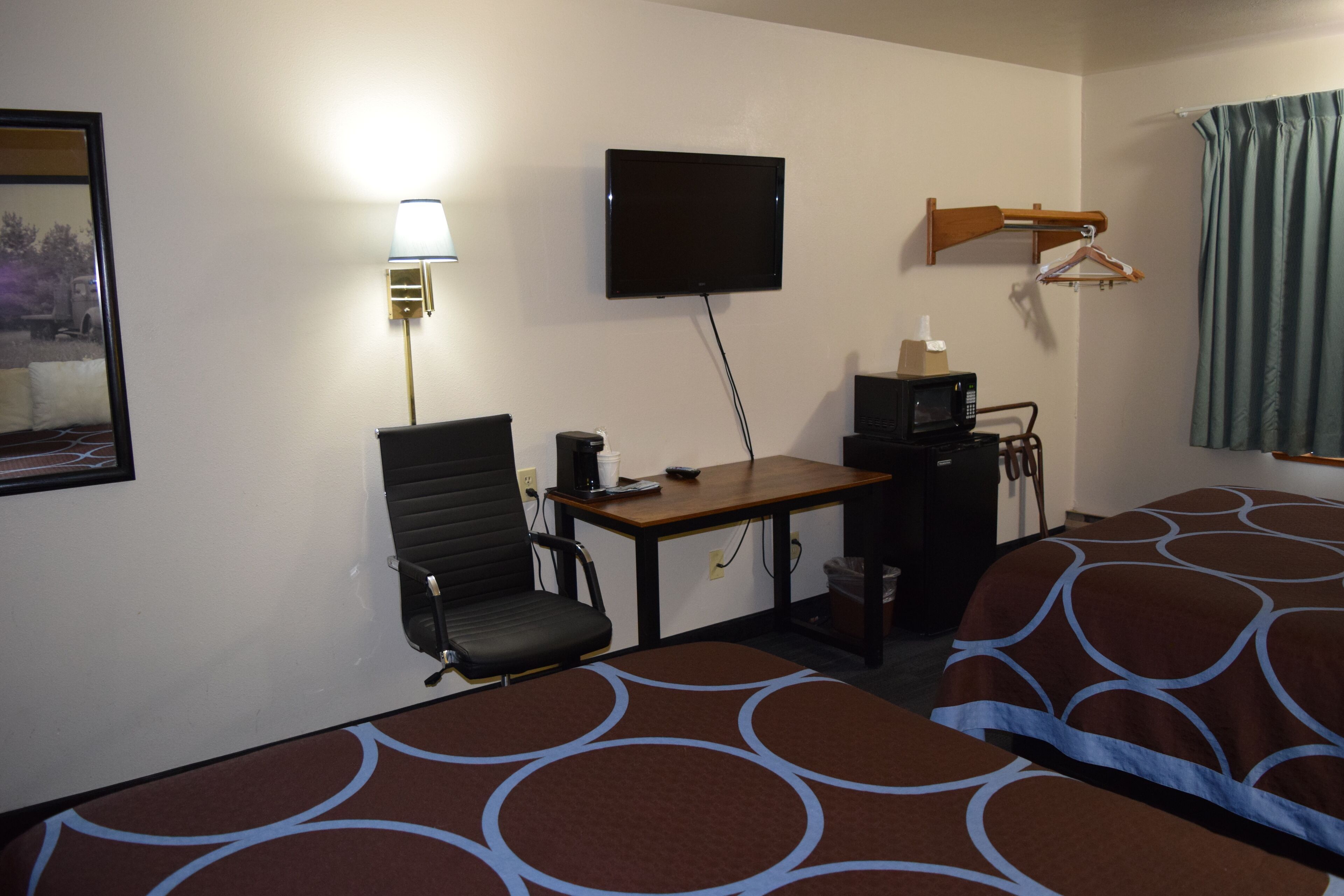 A hotel room with a bed, a desk with a chair, a television, and a lamp.