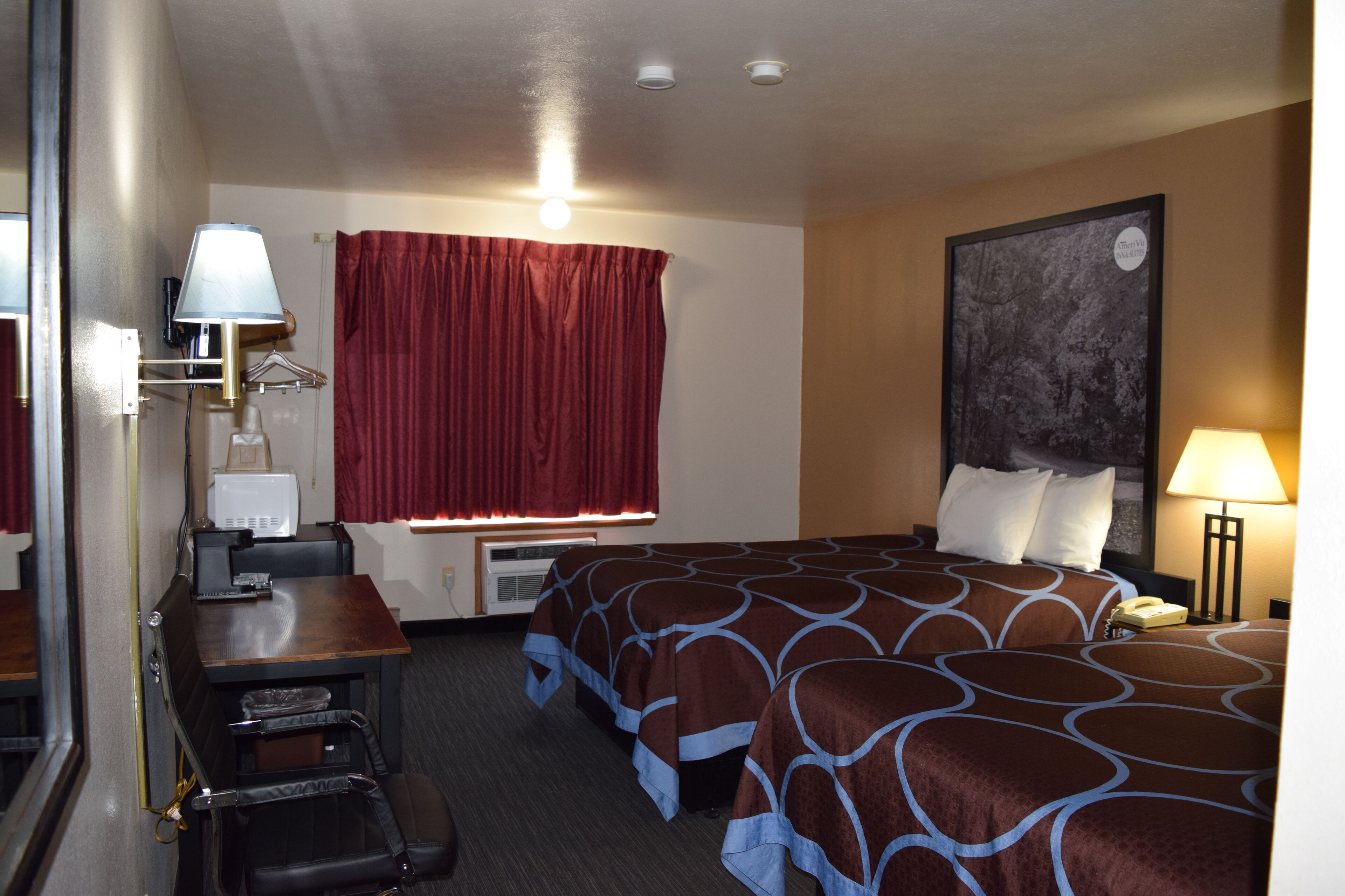 Een hotelkamer met twee bedden, een bureau, een stoel, een lamp, een telefoon en een schilderij aan de muur.