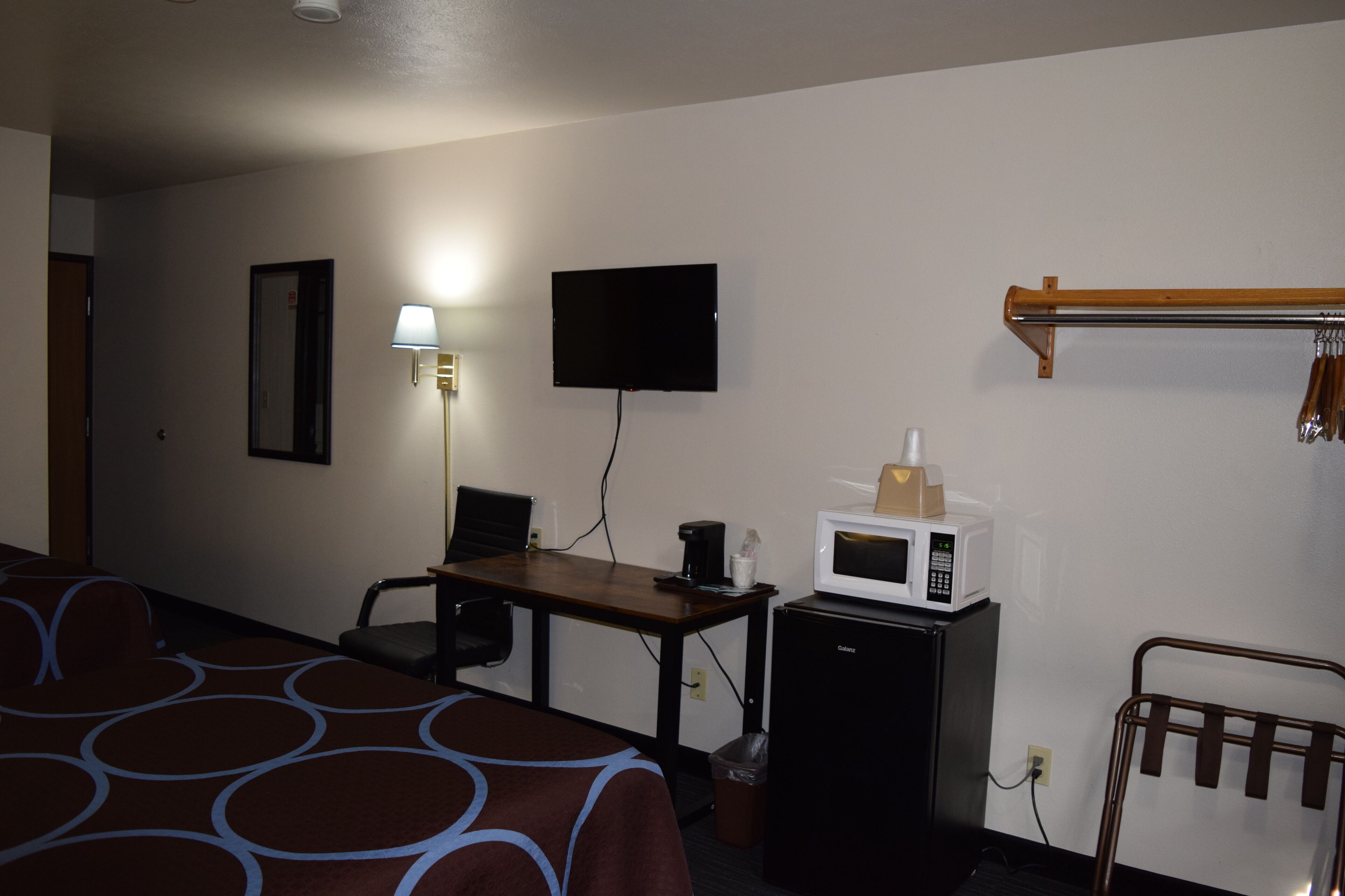 A hotel room with a bed, a desk, a television, a microwave, and a small refrigerator.