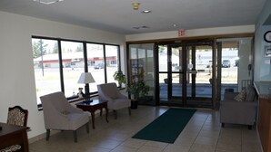 A lobby with two armchairs, a small table, a lamp, a potted plant, and a green mat.