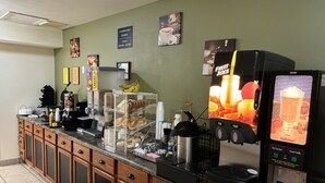 A breakfast bar with a coffee machine, a juice dispenser, and a display of pastries.