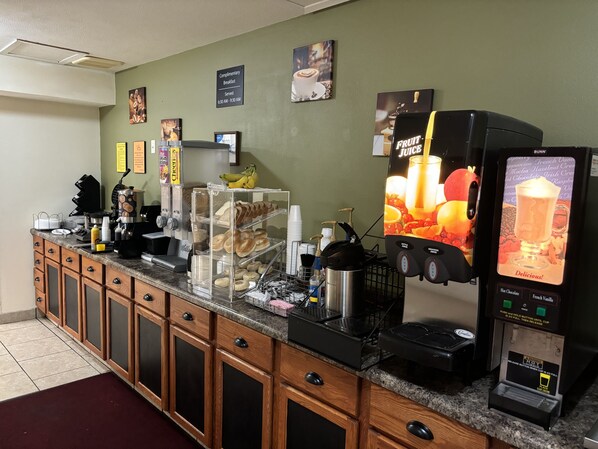 A breakfast bar with a coffee machine, a juice dispenser, and a display of pastries.
