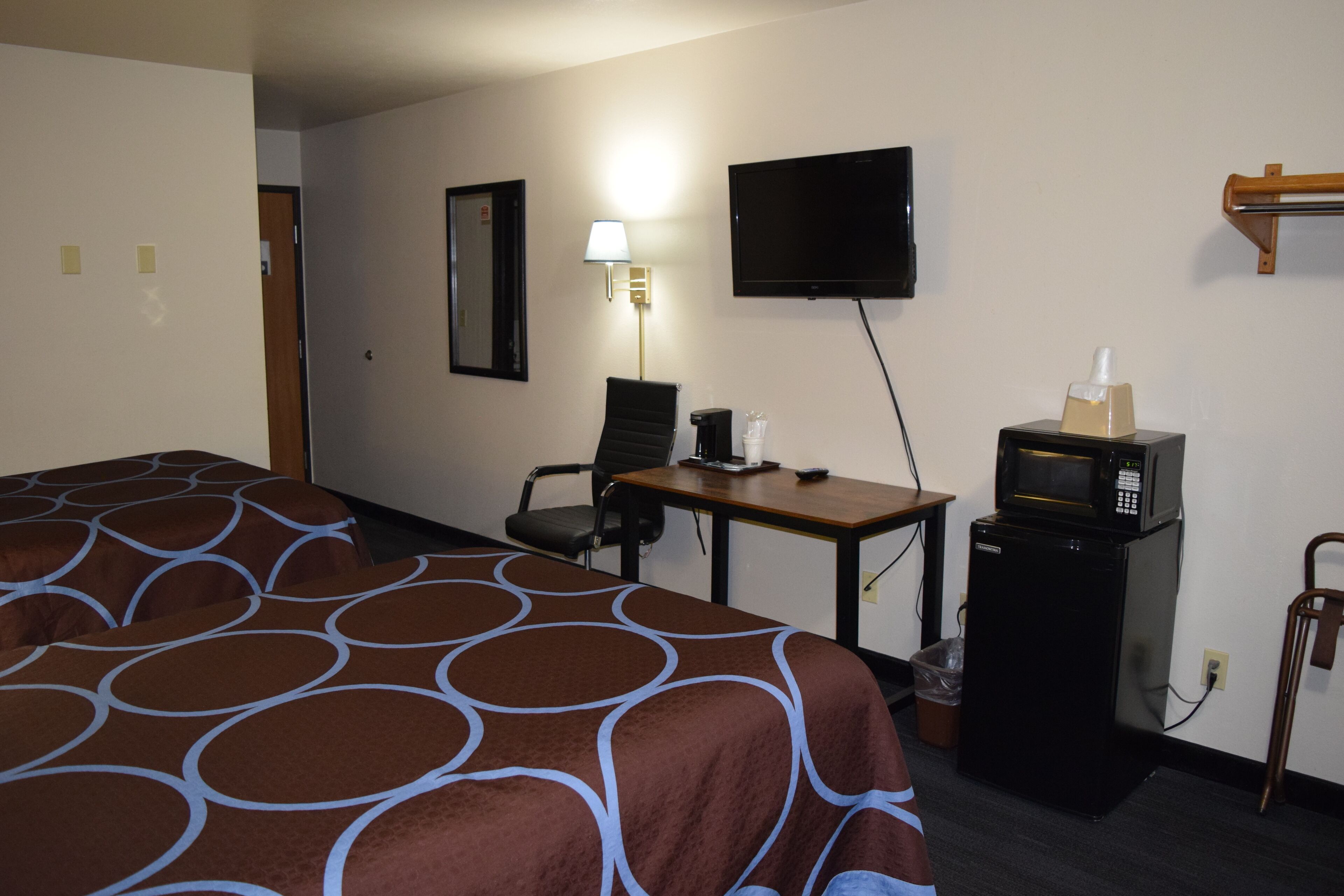 A hotel room with a bed, a desk, a television, a microwave, and a trash can.