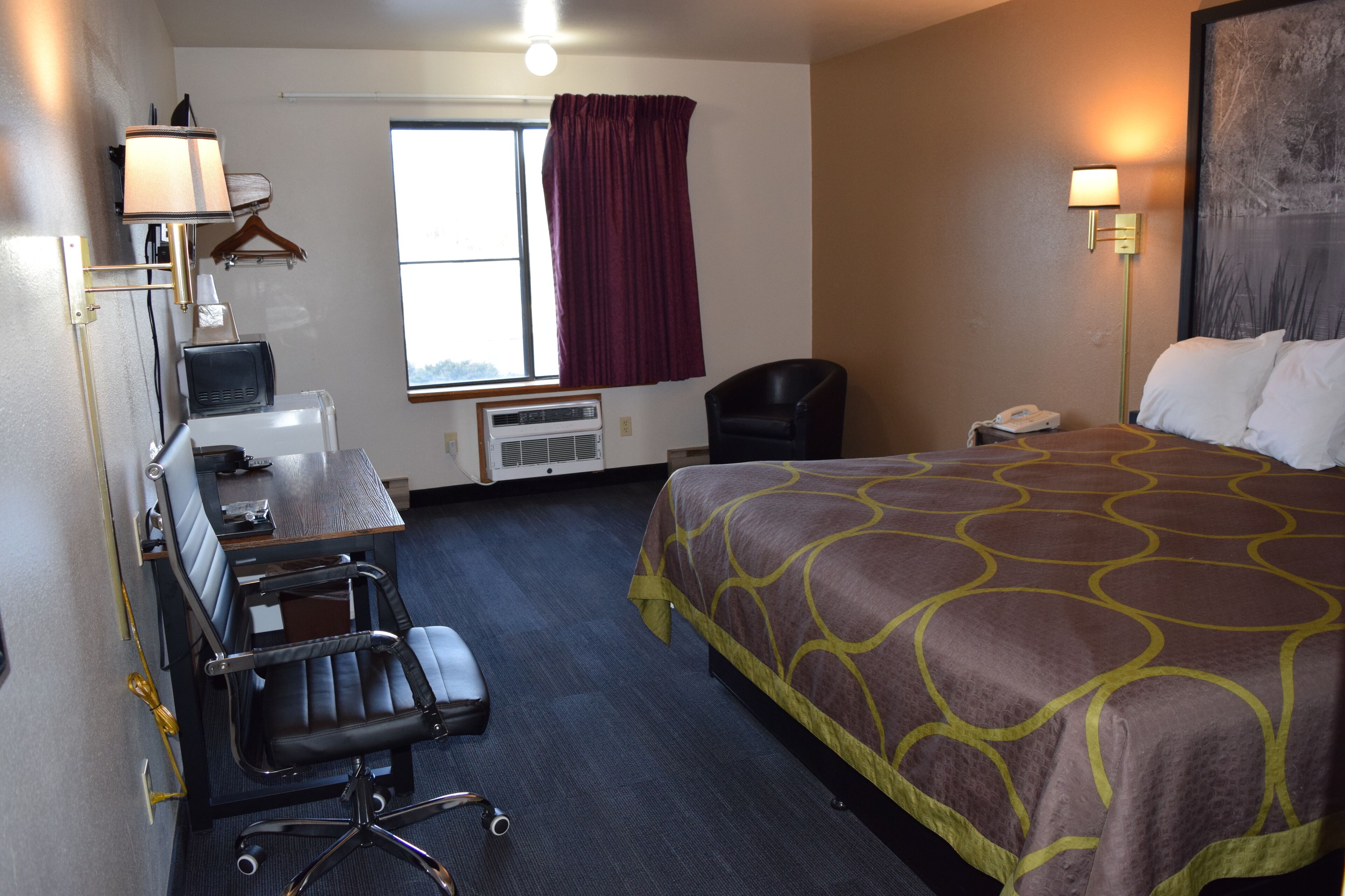 Una habitación de hotel con cama, escritorio, silla y ventana con cortinas.