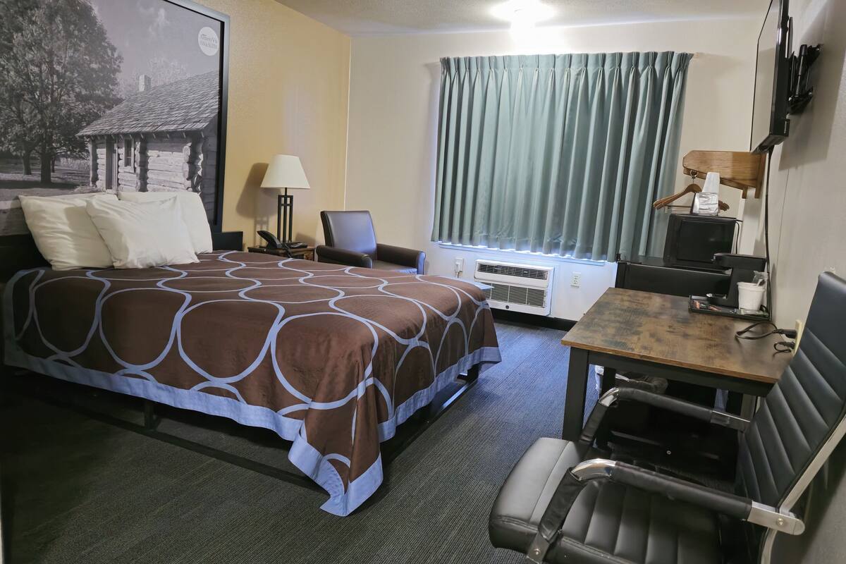 A hotel room with a bed, a desk, a chair, a television, and a window with curtains.