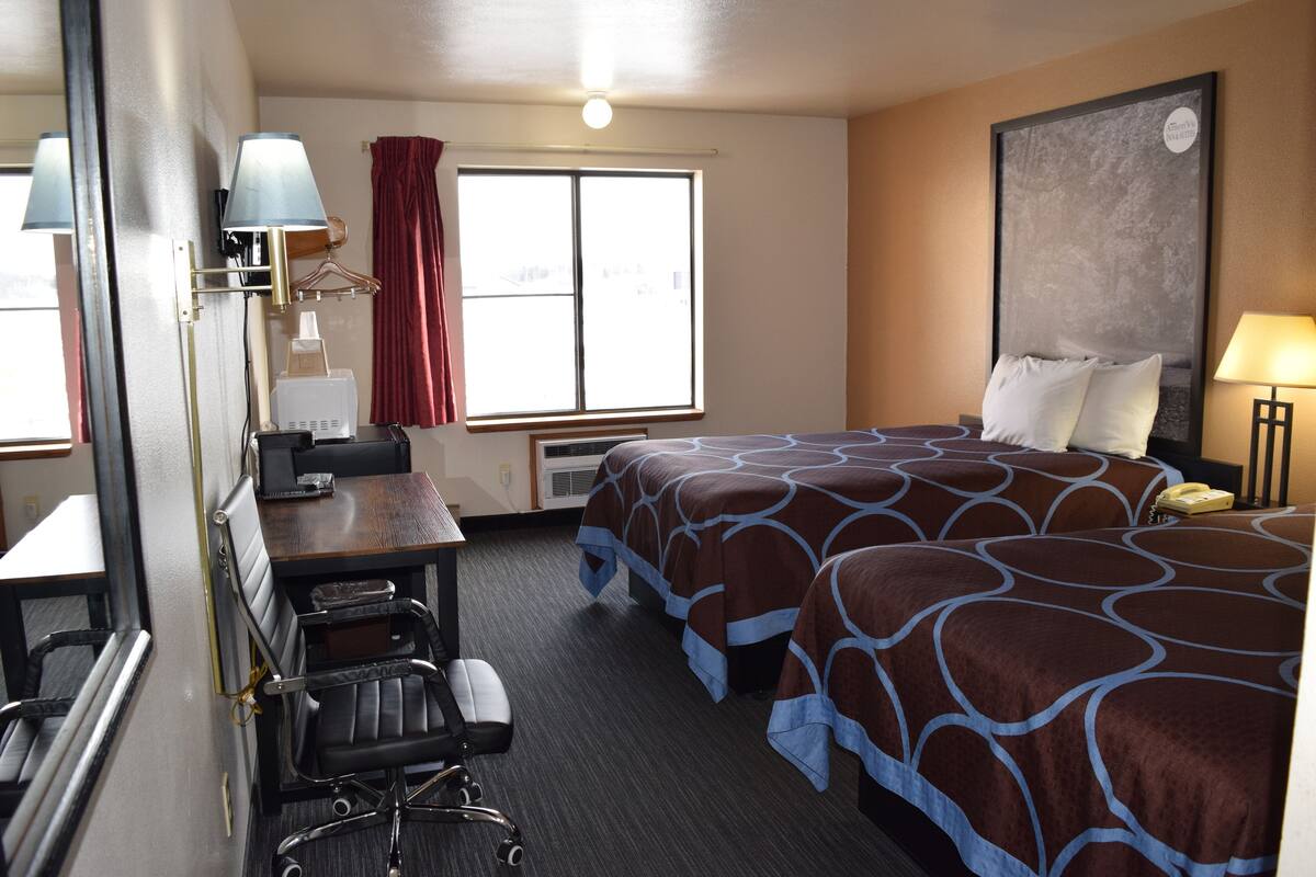 A hotel room with a bed, desk, chair, and a window with curtains.