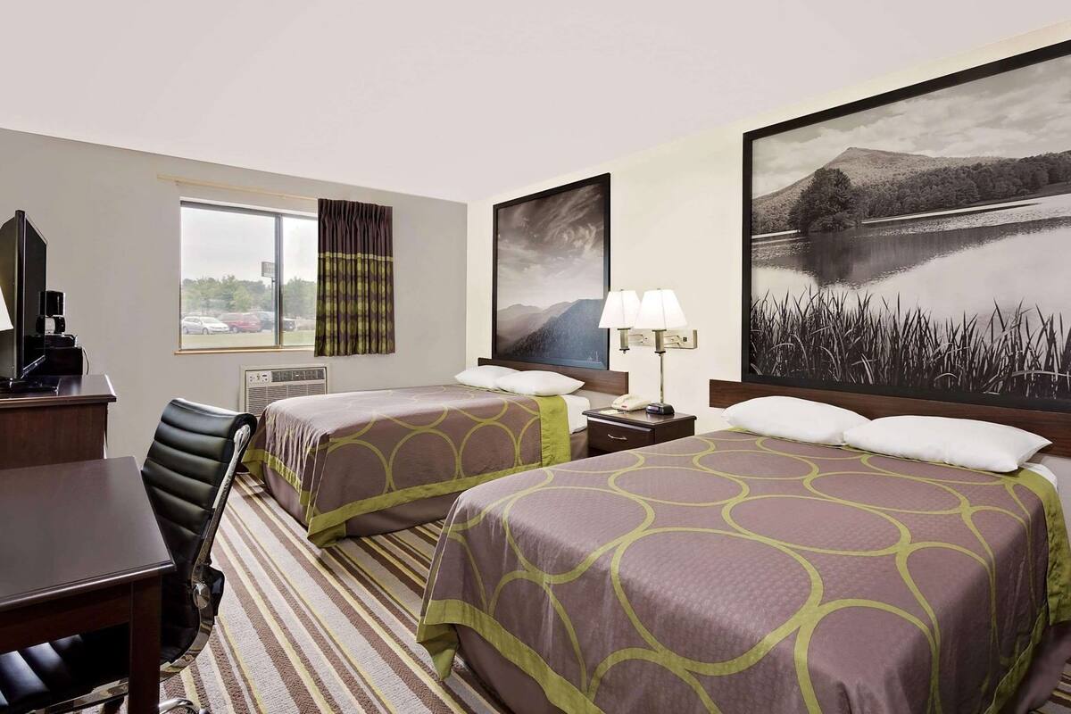 A hotel room with two beds, a desk, a chair, a TV, and a large window.
