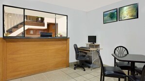 Un área de recepción con un escritorio de madera, una computadora y un televisor. Se observa una escalera al fondo, y dos cuadros en la pared.