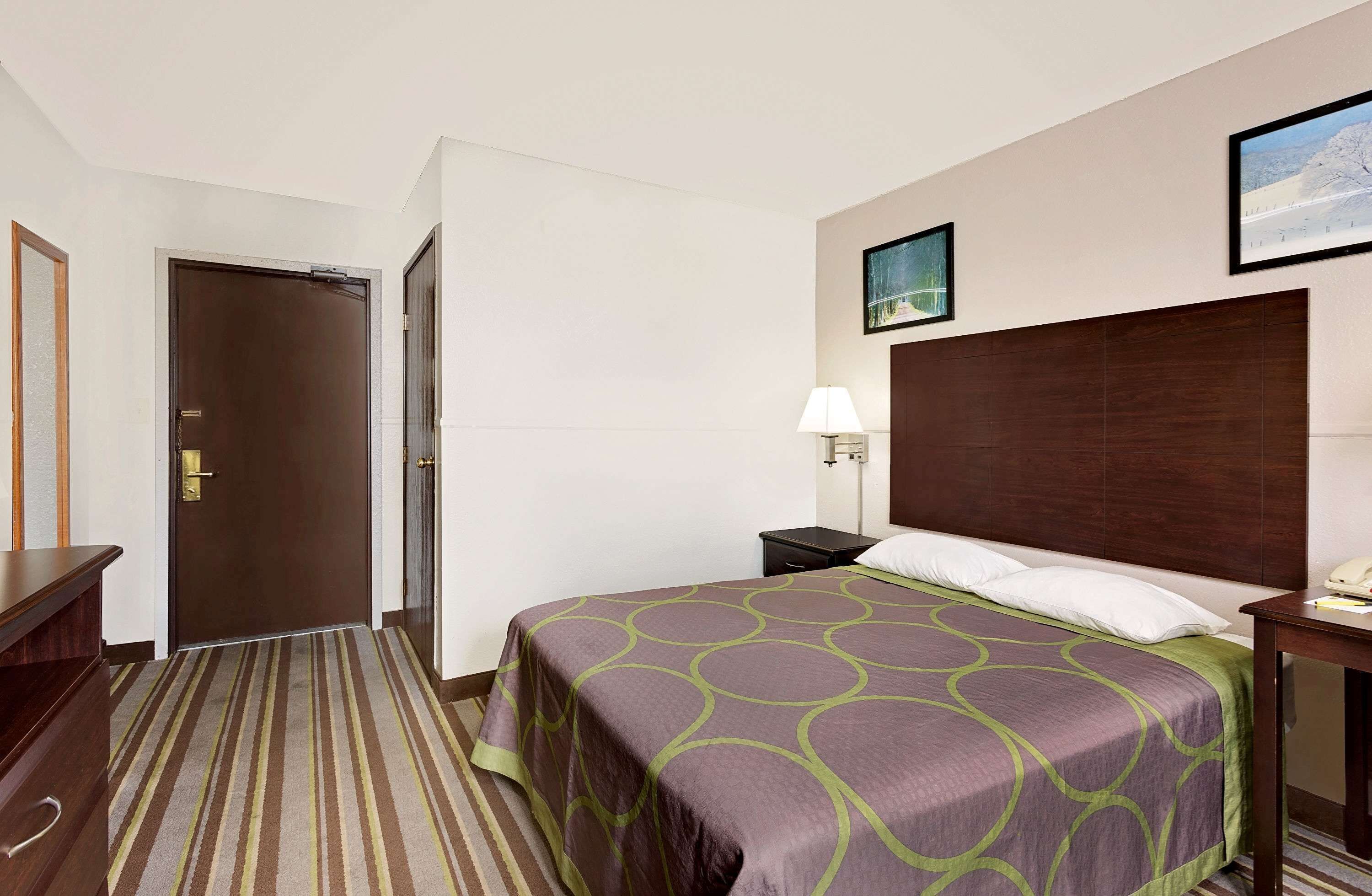 A hotel room with a bed, a nightstand, a lamp, and a painting on the wall.
