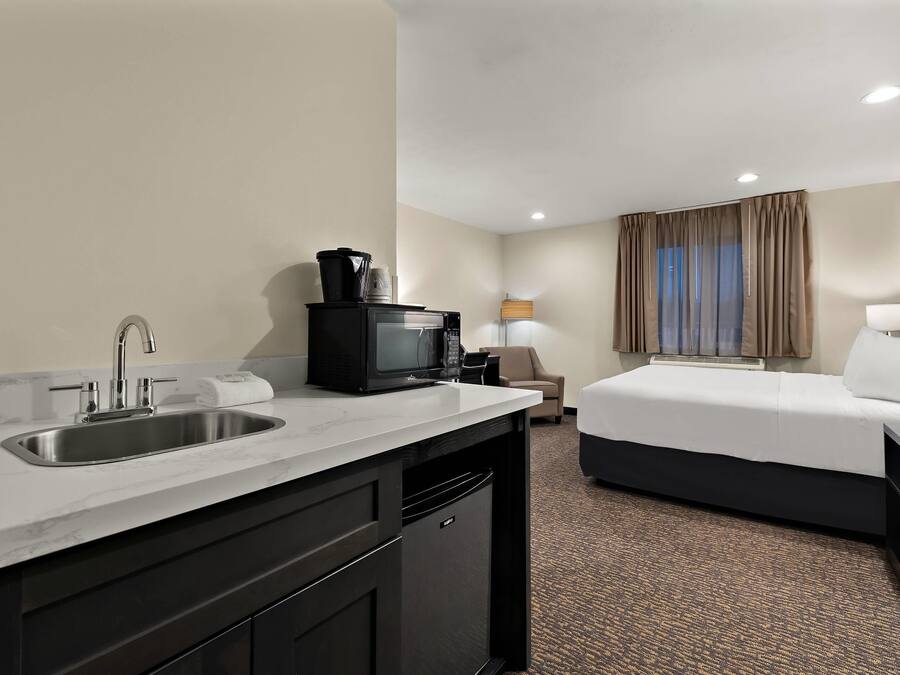 A hotel room with a kitchenette, a bed, a desk, and a lamp.