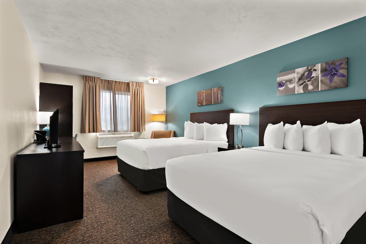 A hotel room with two beds, a desk, a TV, and a window with curtains.
