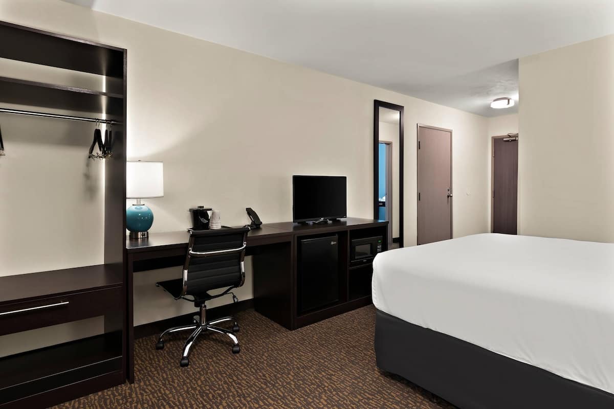 A hotel room with a bed, a desk with a computer, a chair, a TV, and a microwave.