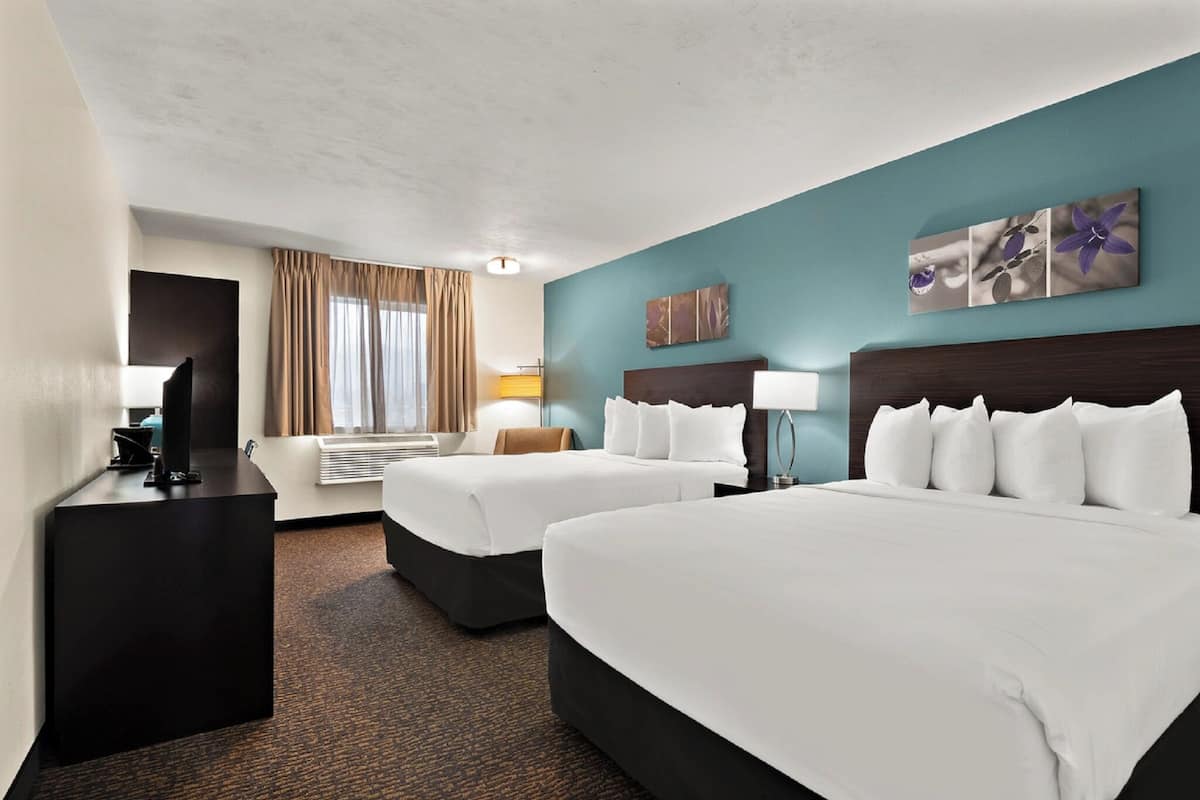 A hotel room with two beds, a desk, a TV, and artwork on the walls.