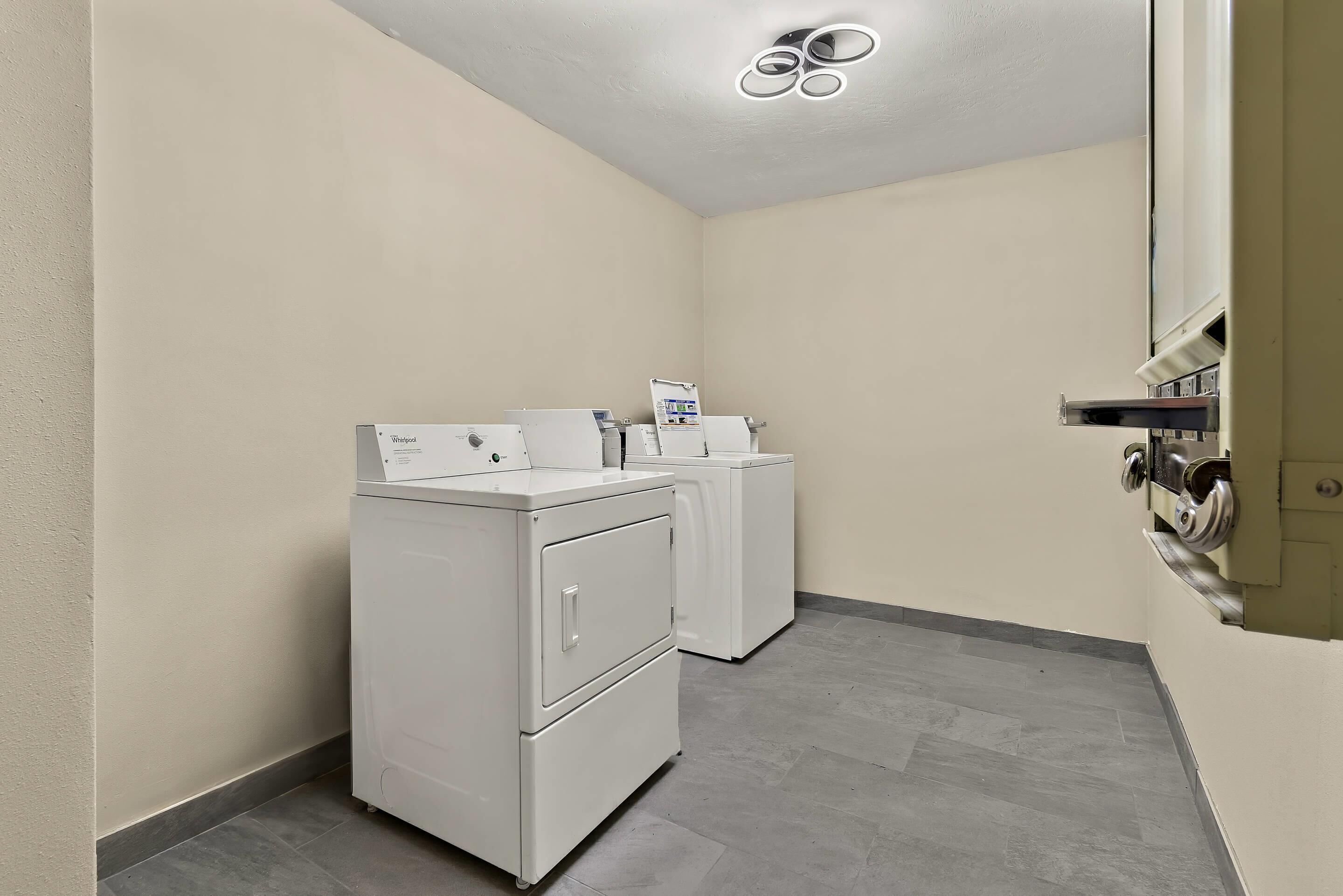 A laundry room with two stacked washers and dryers, a ceiling light fixture, and a wall-mounted utility cabinet.