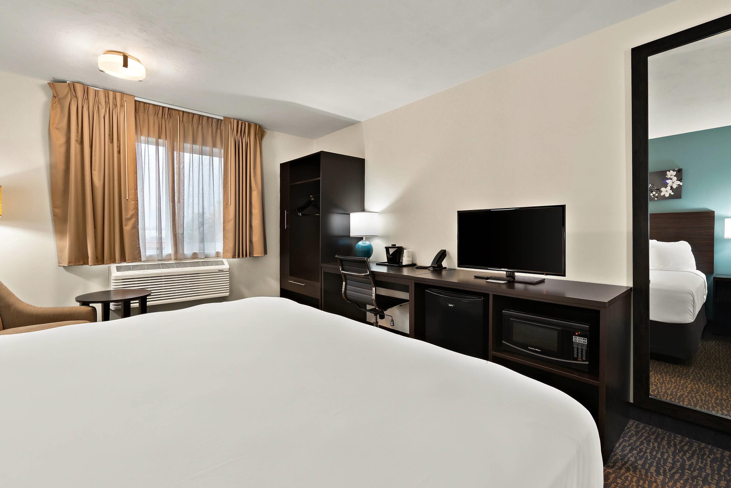 Een hotelkamer met een groot bed, een bureau met een televisie, een stoel, een kleine tafel, een magnetron en een kledingkast.