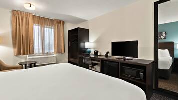Een hotelkamer met een groot bed, een bureau met een televisie, een stoel, een kleine tafel, een magnetron en een kledingkast.