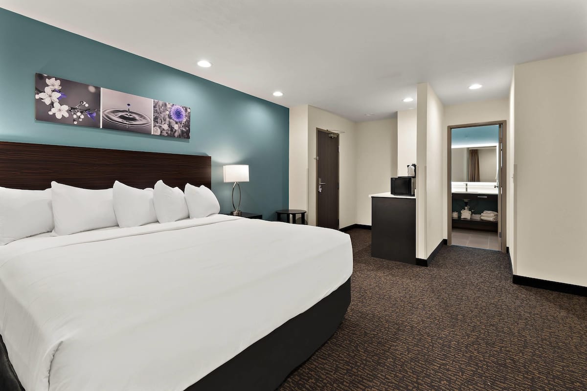 A hotel room with a large bed, a desk, a chair, a mirror, and a door leading to a bathroom.