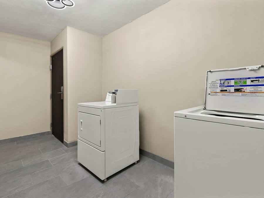 A laundry room with a front-loading washer and dryer, a door, and a wall-mounted instruction manual.