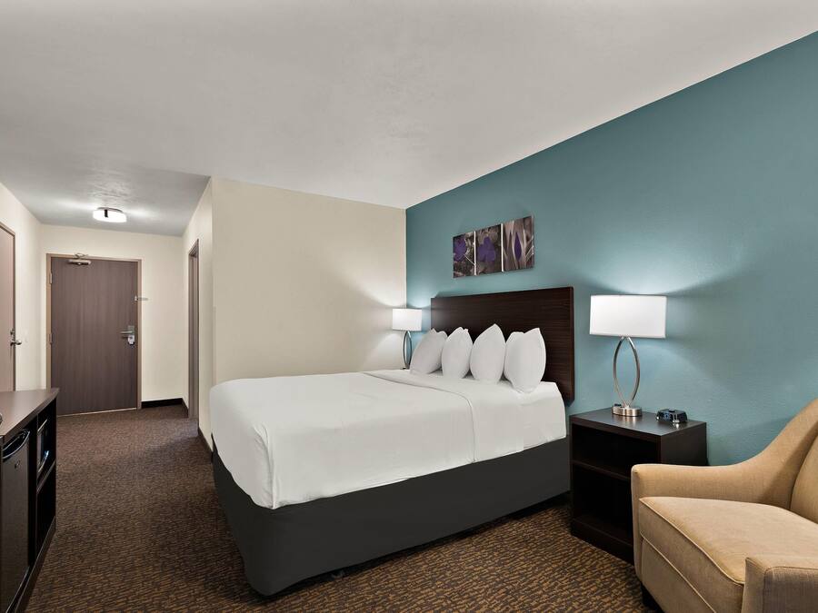 Una habitación de hotel con cama, escritorio, silla y mesita de noche con lámpara.