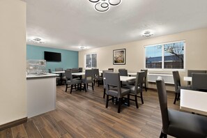 A restaurant with multiple tables and chairs, a flat-screen TV mounted on the wall, and a window with blinds.