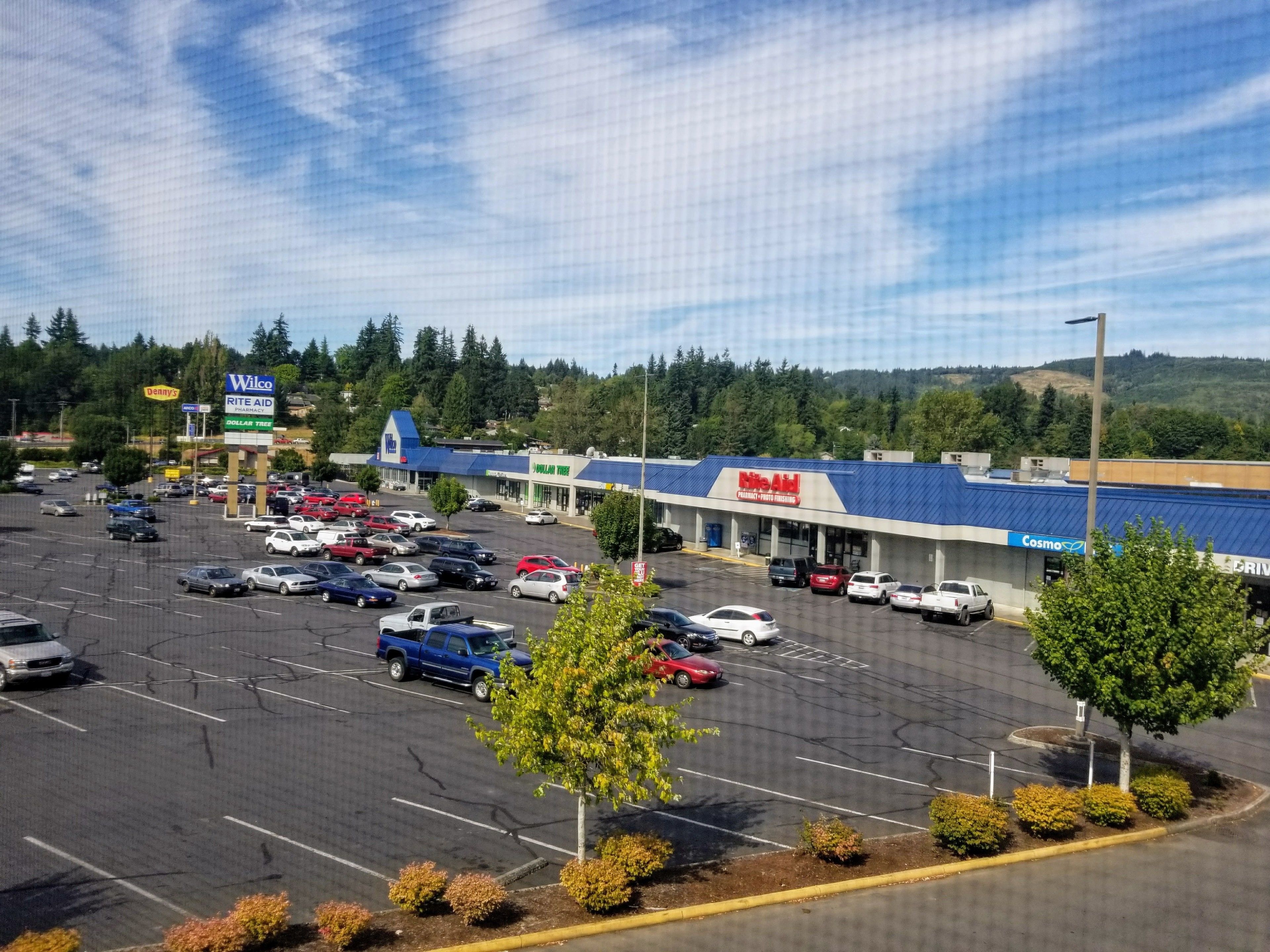 Un estacionamiento con varios autos y un edificio grande con techo azul y una farmacia Rite Aid.