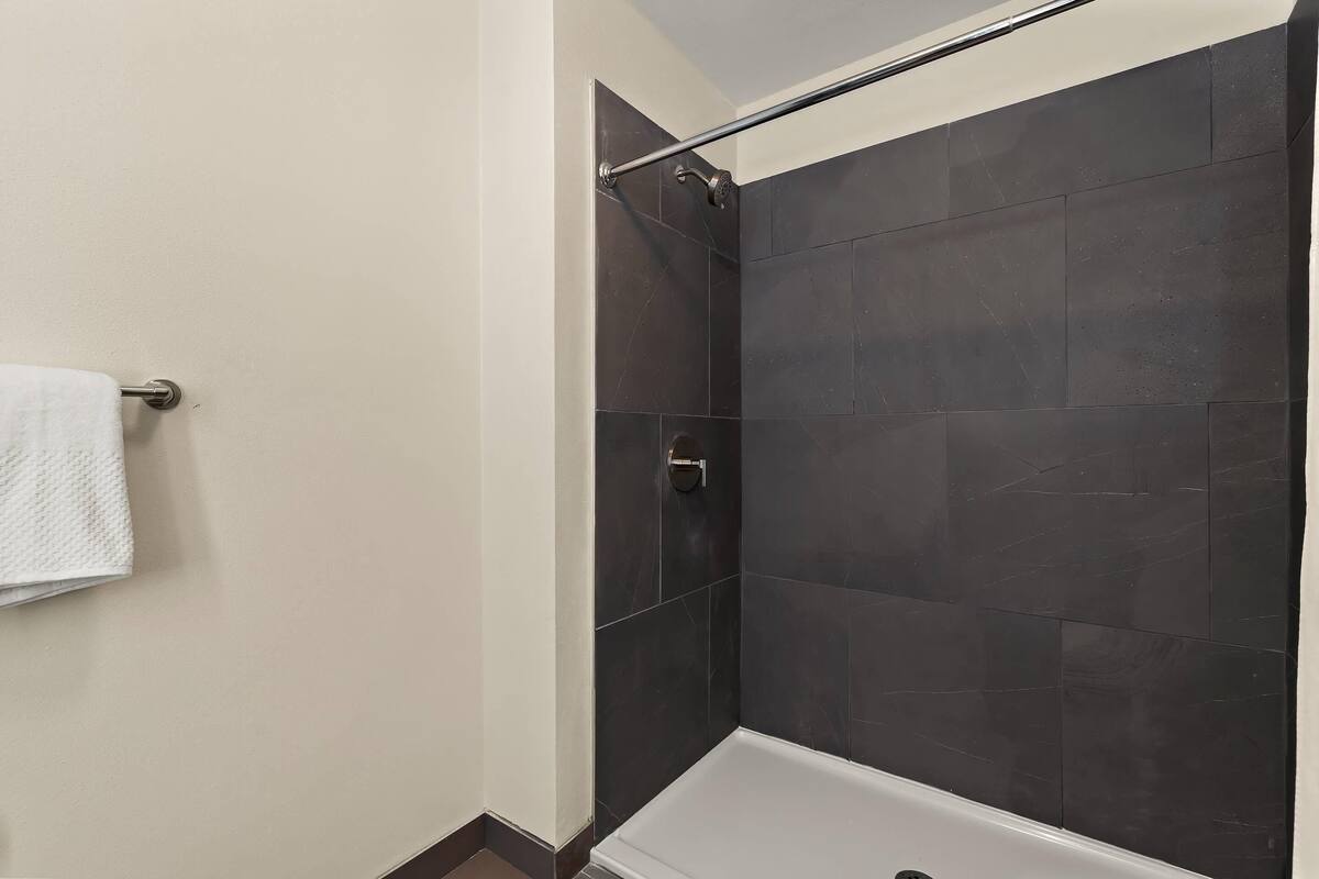 A bathroom with a shower, dark tiled walls, and a white towel on a rack.