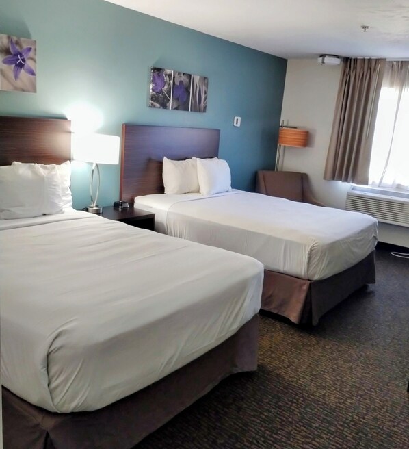 Two single beds with wooden headboards and white bedding, a blue accent wall, and a floral artwork adorn this inviting space.