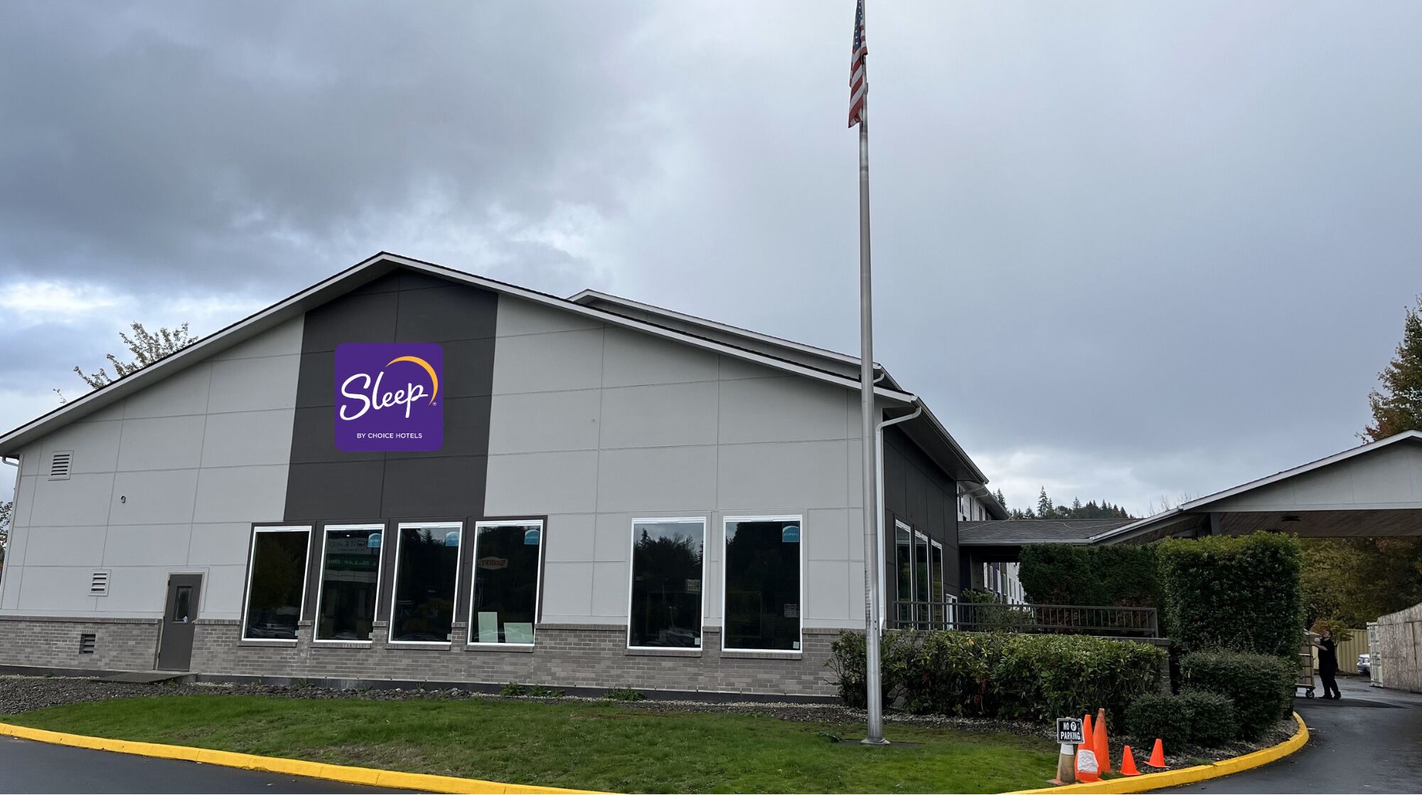 A Sleep by Choice Hotels building with a large sign, a flagpole, and a parking area with cones.