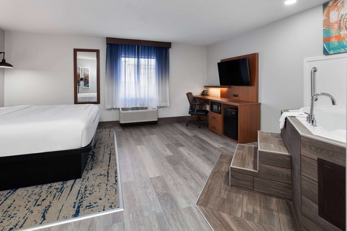 A hotel room with a bed, desk, TV, and bathroom.