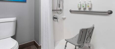 A bathroom with a white toilet, a shower with a handheld showerhead, a grab bar, and three bottles of Dove soap on a shelf.
