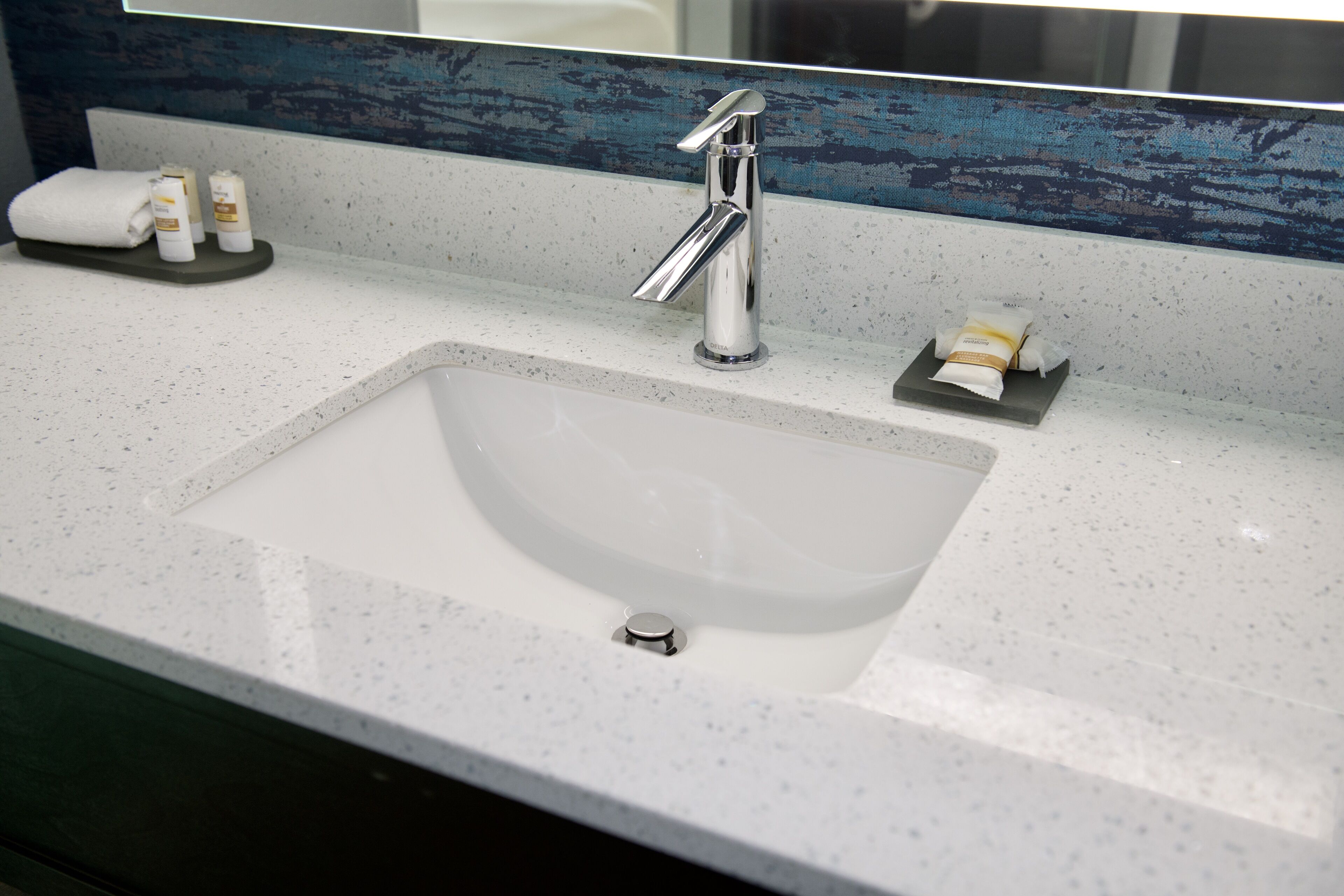 A bathroom sink with a chrome faucet, a towel, and toiletries on the countertop.