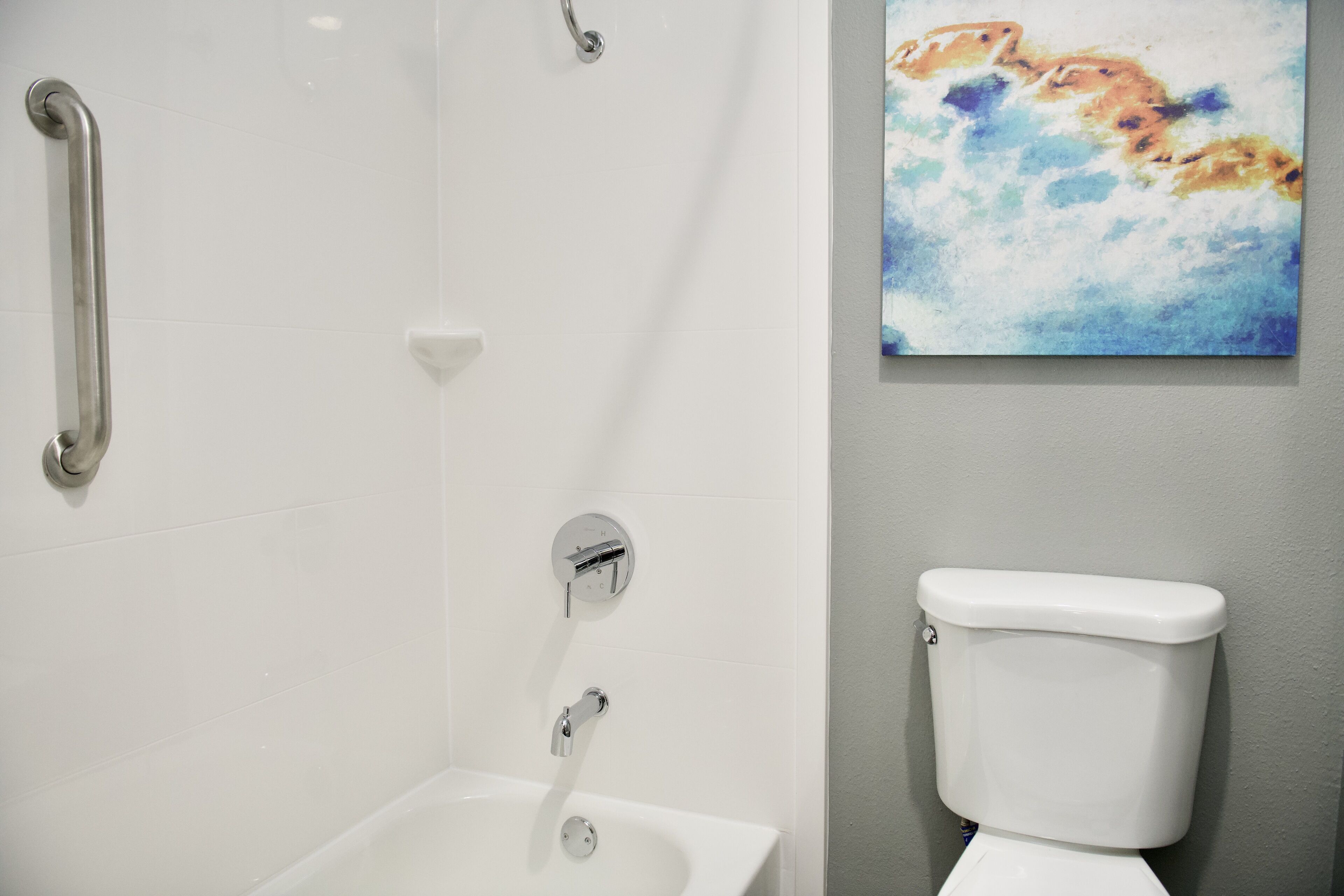 Un baño con una bañera blanca, un inodoro blanco y un pasamanos.