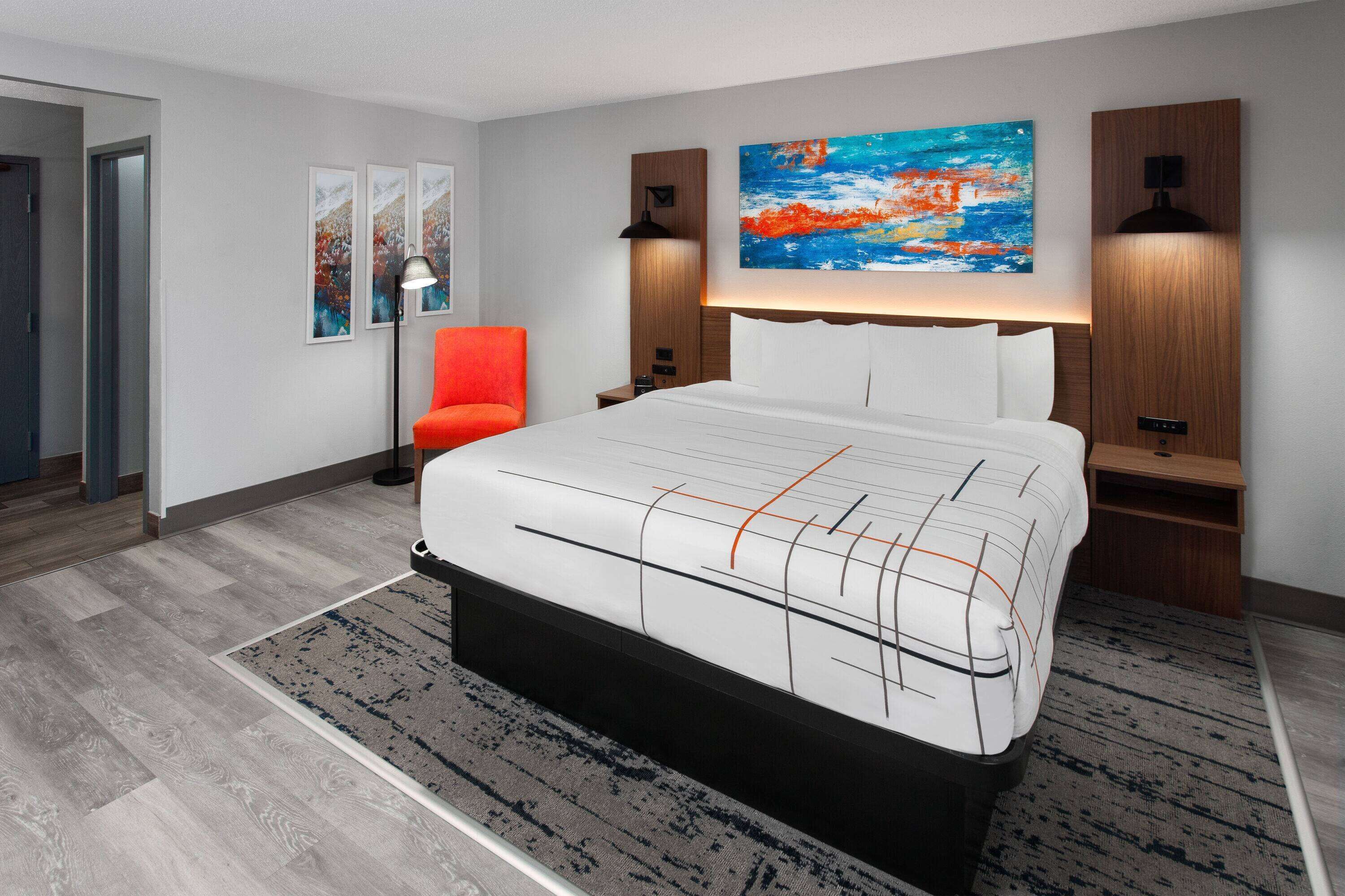 Une chambre d’hôtel moderne avec un grand lit, un fauteuil rouge et des œuvres d’art accrochées aux murs.