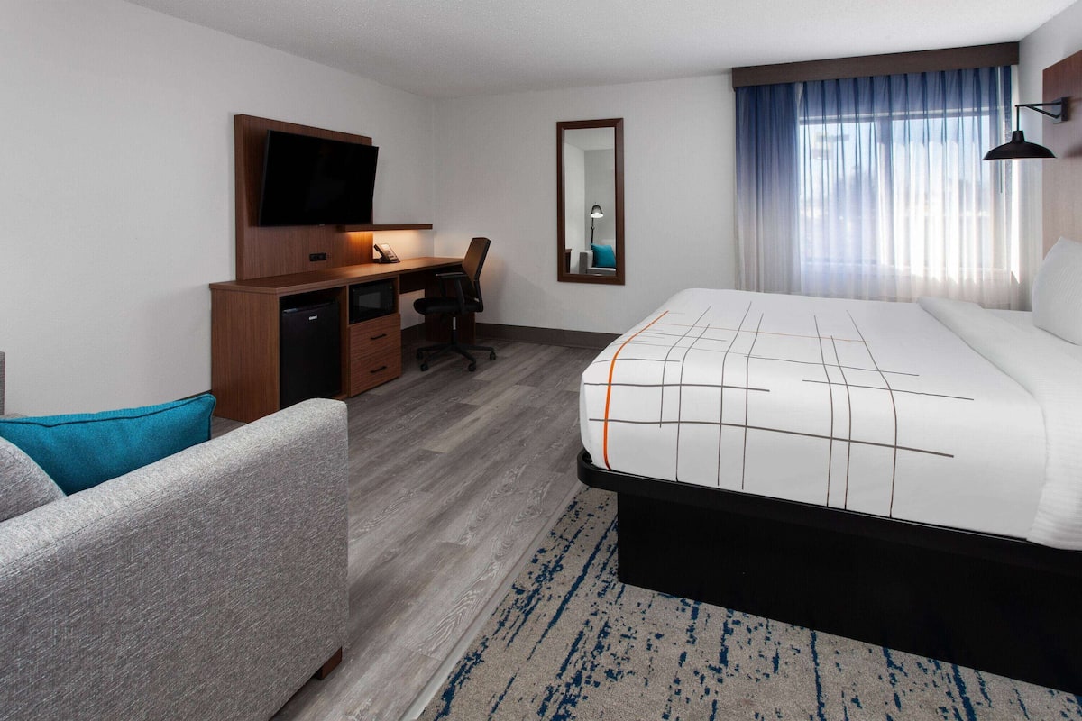 A hotel room with a bed, a desk with a chair, a television, and a mirror.