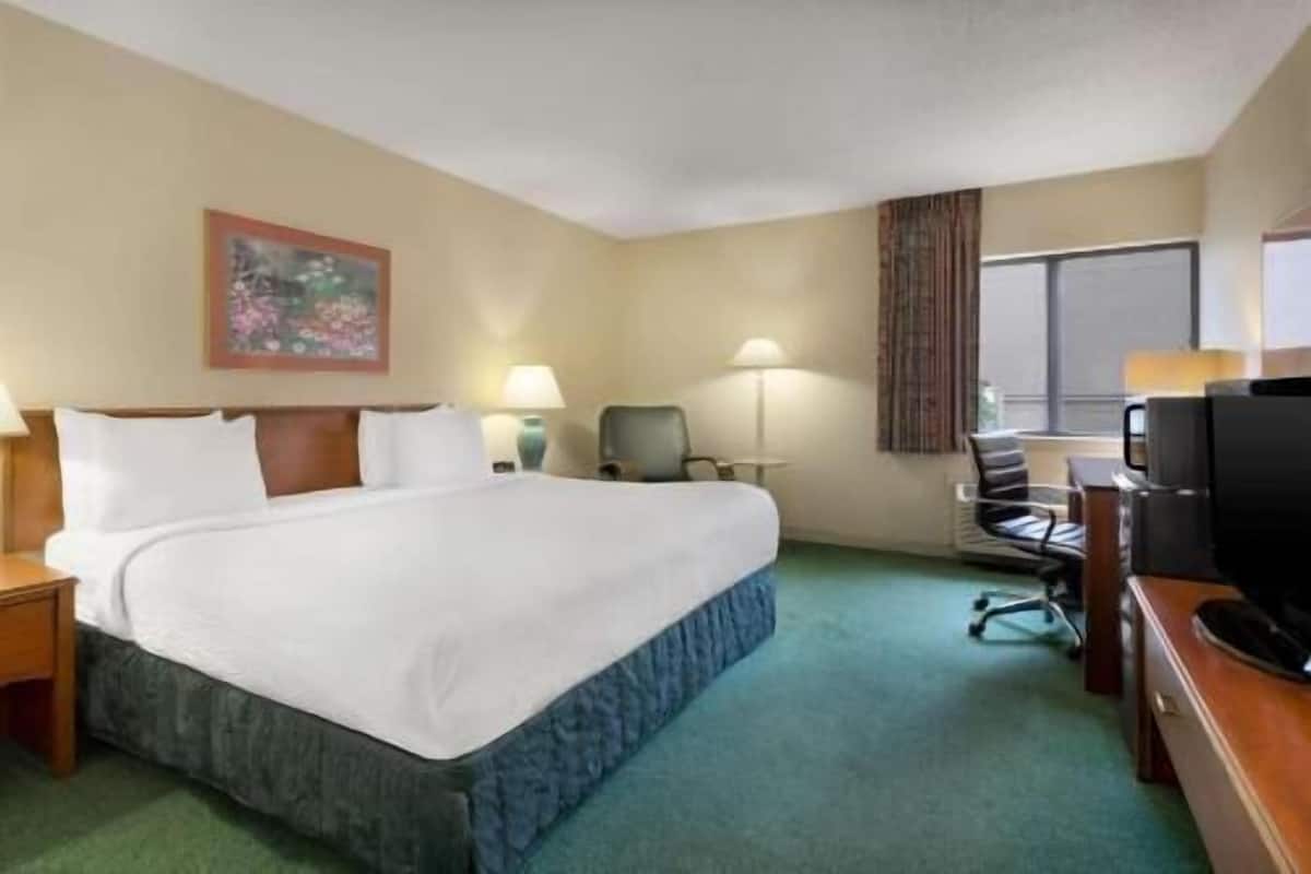 A hotel room with a large bed, a desk with a computer, a chair, a TV, and a painting on the wall.