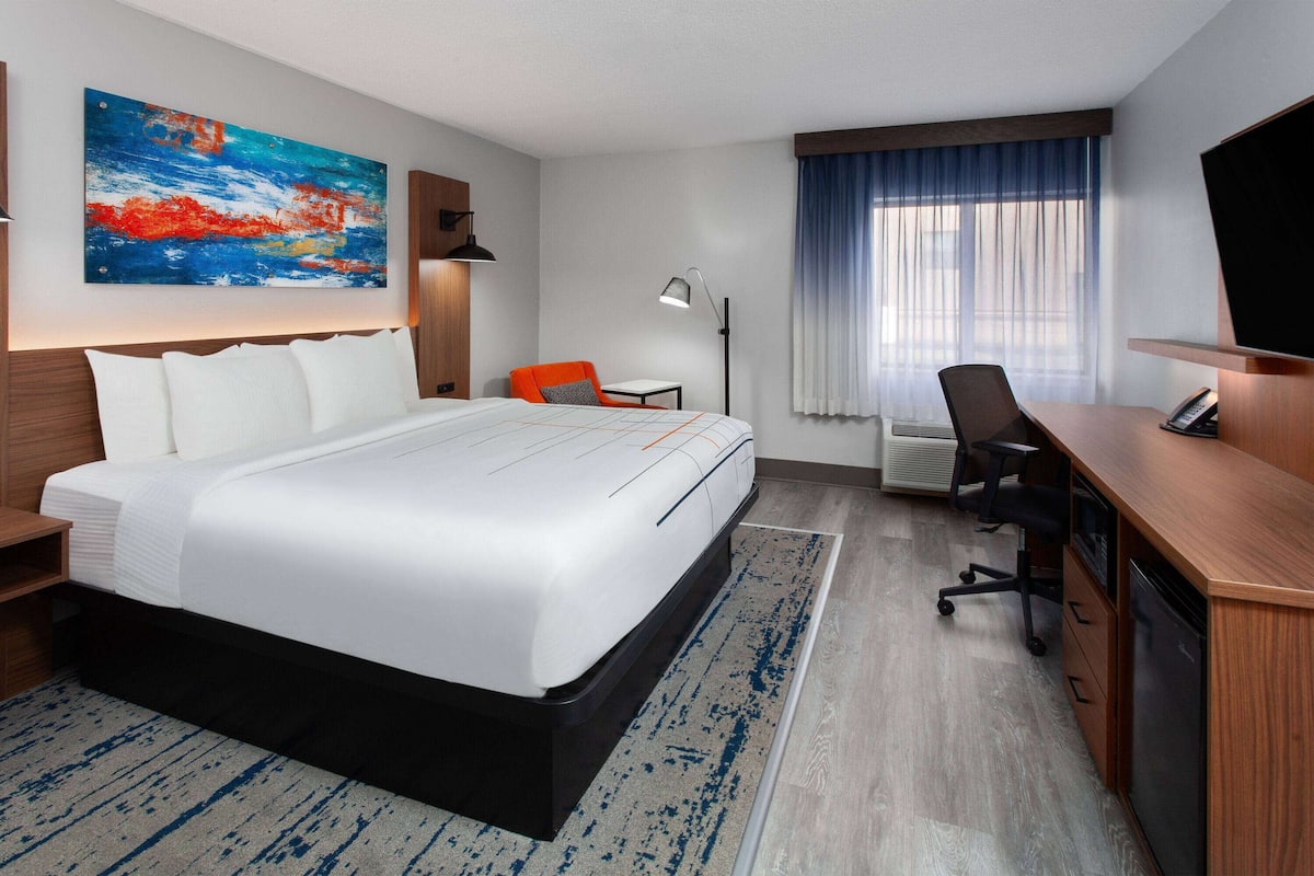 A hotel room with a large bed, a desk, a chair, a TV, and a painting on the wall.