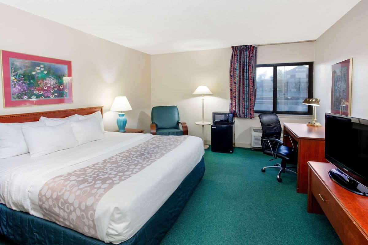 Una habitación de hotel con una cama grande, un escritorio con computadora, un televisor y una ventana con cortinas.