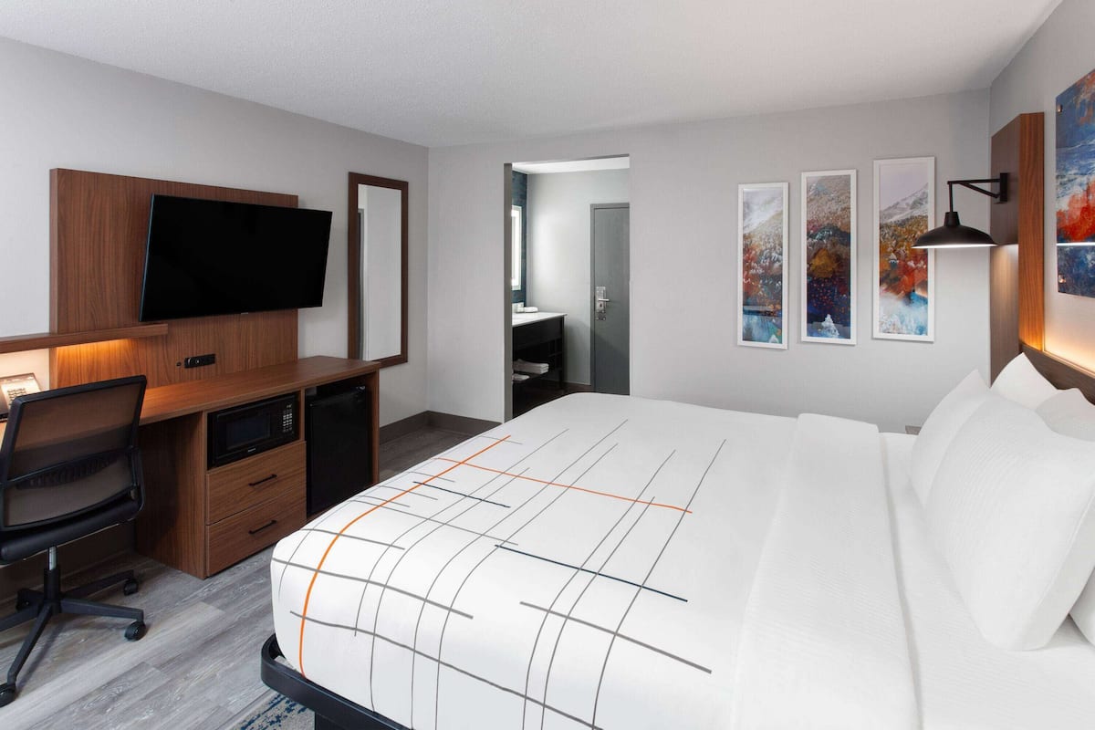 A modern hotel room with a large bed, a desk with a flat-screen TV, a microwave, and a chair. There are three framed pictures on the wall.