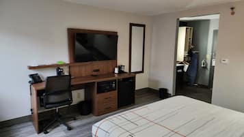 Habitación de hotel con escritorio de madera, televisor de pantalla plana, cama con colcha estampada, microondas y un pequeño cubo de basura.