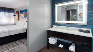 Una habitación de hotel moderna con una cama, un espejo grande, un lavamanos y un tocador de madera oscura.