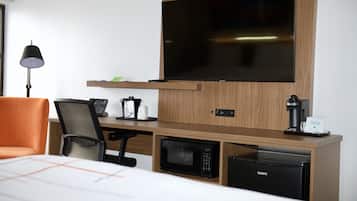 Ein Hotelzimmer mit einem Bett, einem Schreibtisch mit Computer, einer Mikrowelle, einer Kaffeemaschine, einem Fernseher und einer Lampe.