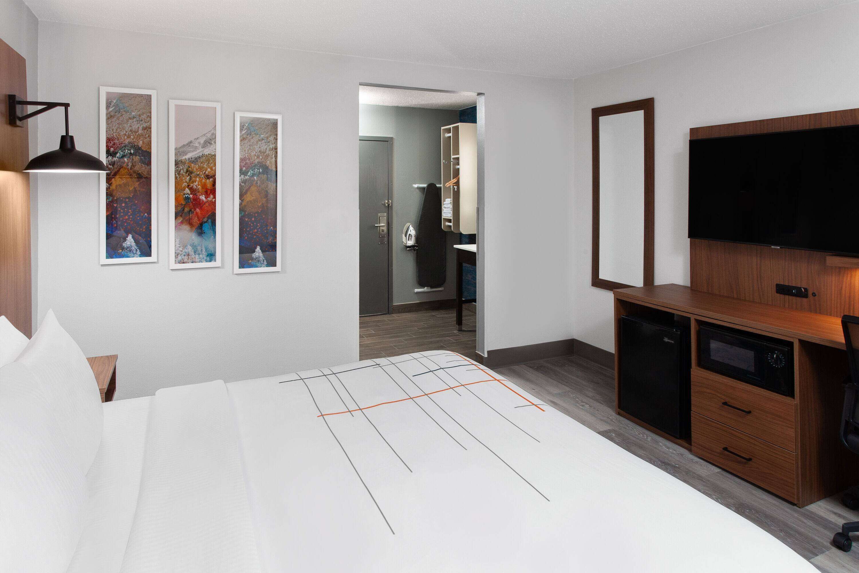 Une chambre d’hôtel comprenant un lit, un bureau avec une télévision, une armoire et des œuvres d’art accrochées au mur.