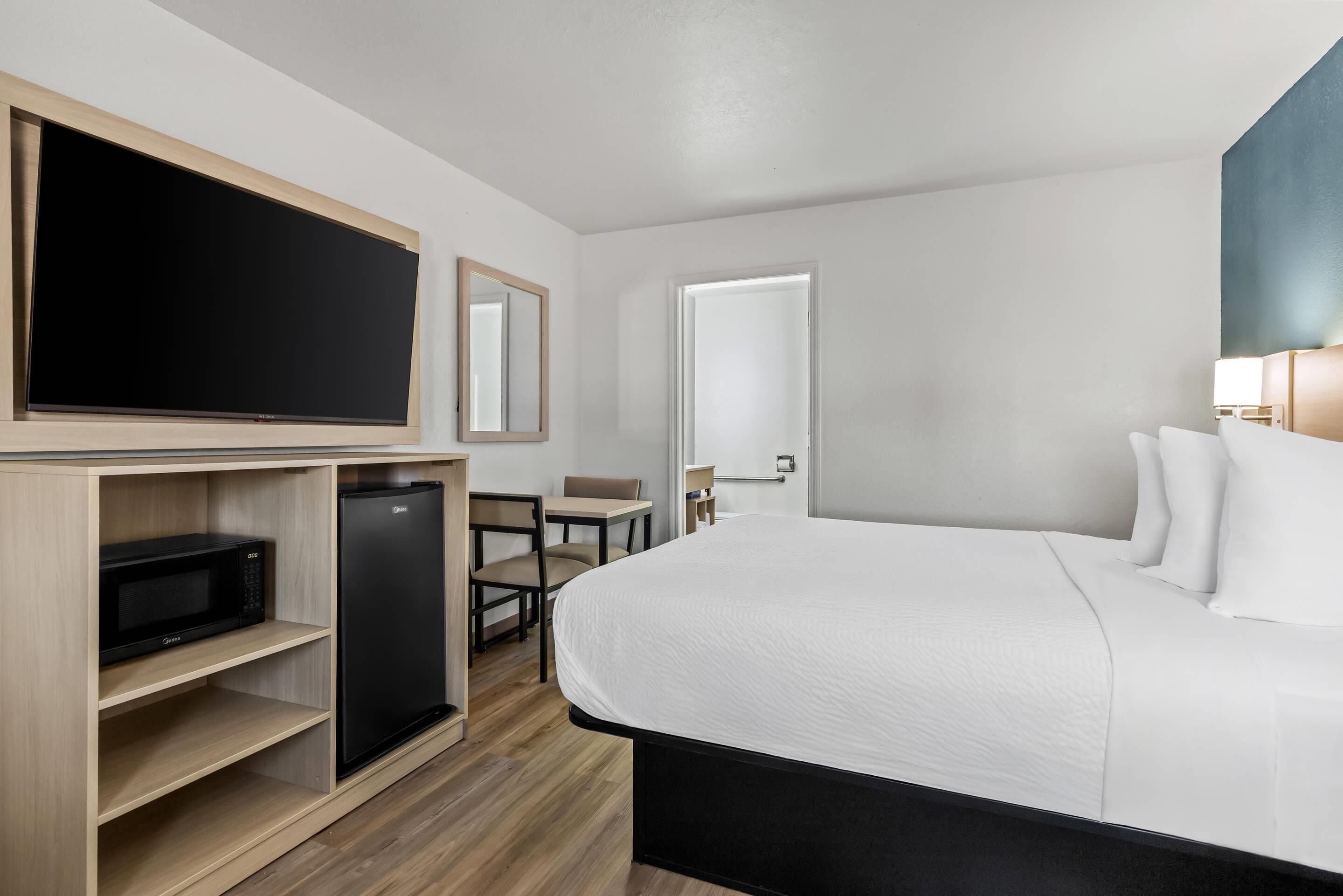 Et hotelværelse med seng, fjernsyn, minibar, skrivebord og stol.