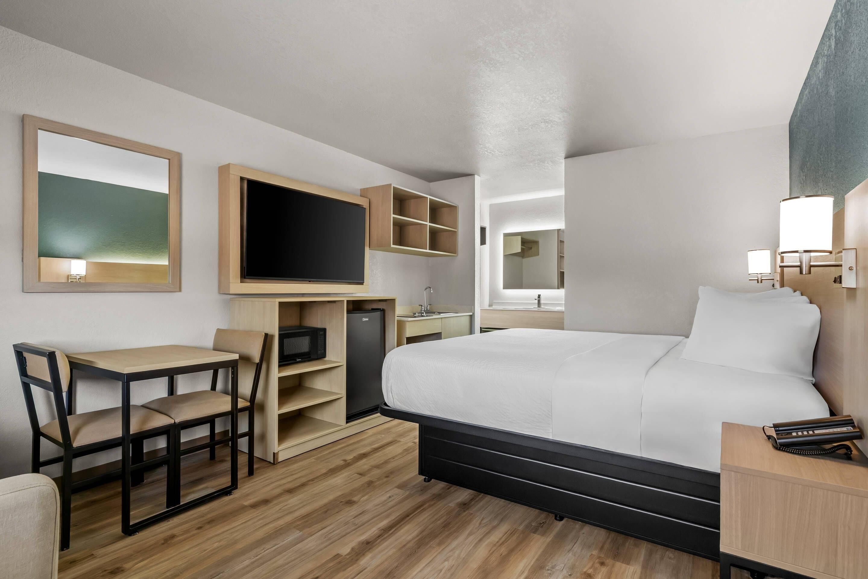 Een moderne hotelkamer met een groot bed, een bureau met stoel, een televisie en een kleine kitchenette.