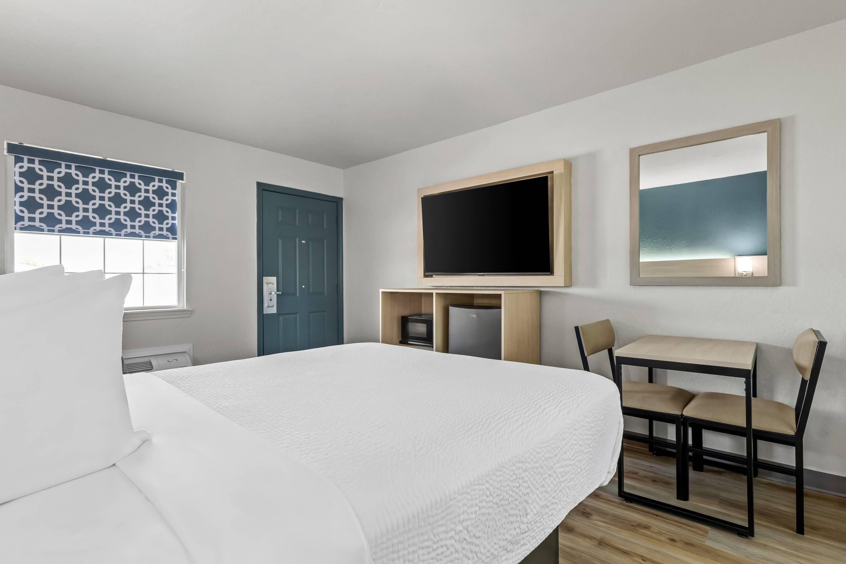 Habitación de hotel con cama, escritorio, silla, televisor y puerta.