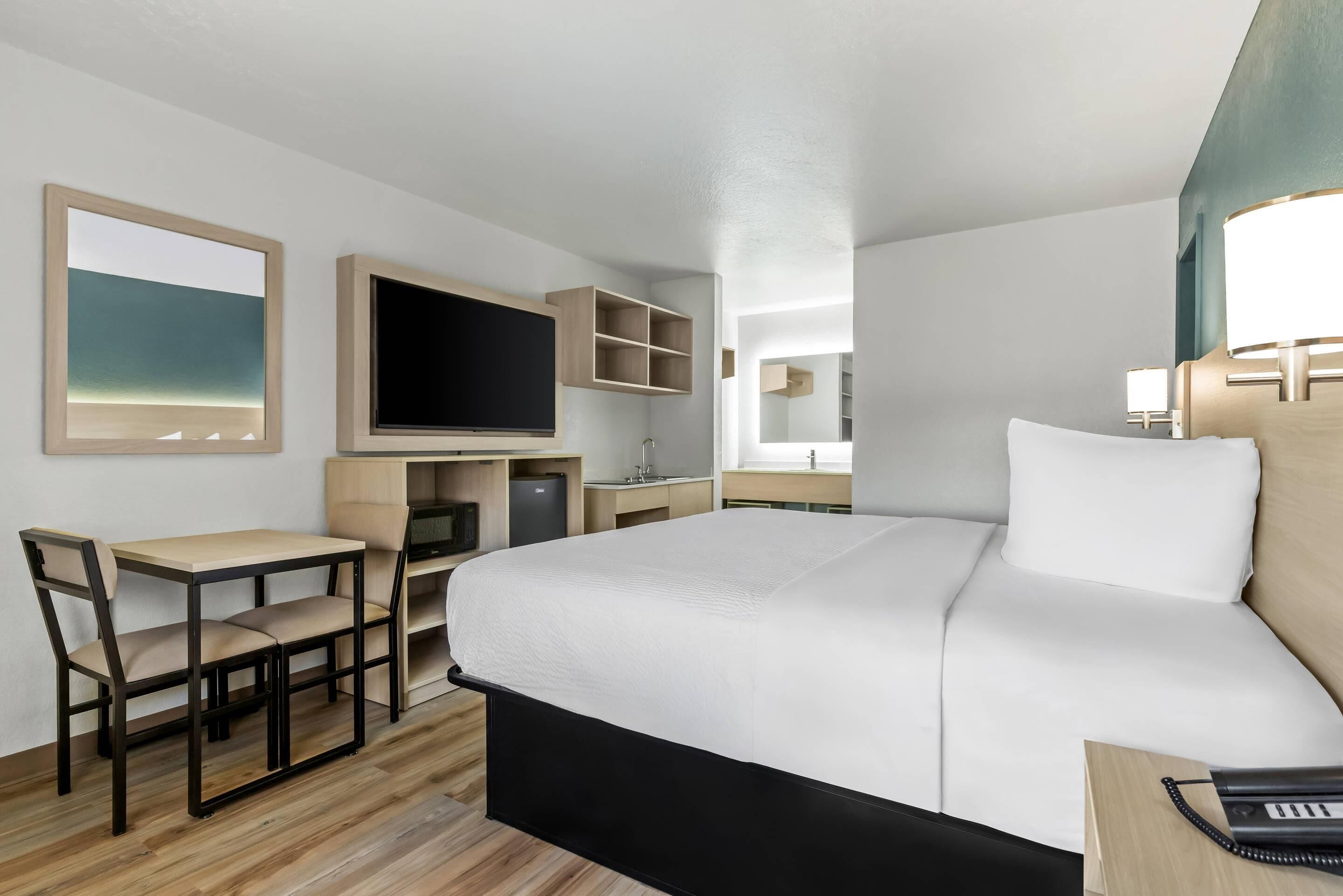 Ein Hotelzimmer mit Bett, Schreibtisch, Fernseher und einer kleinen Küchenzeile.