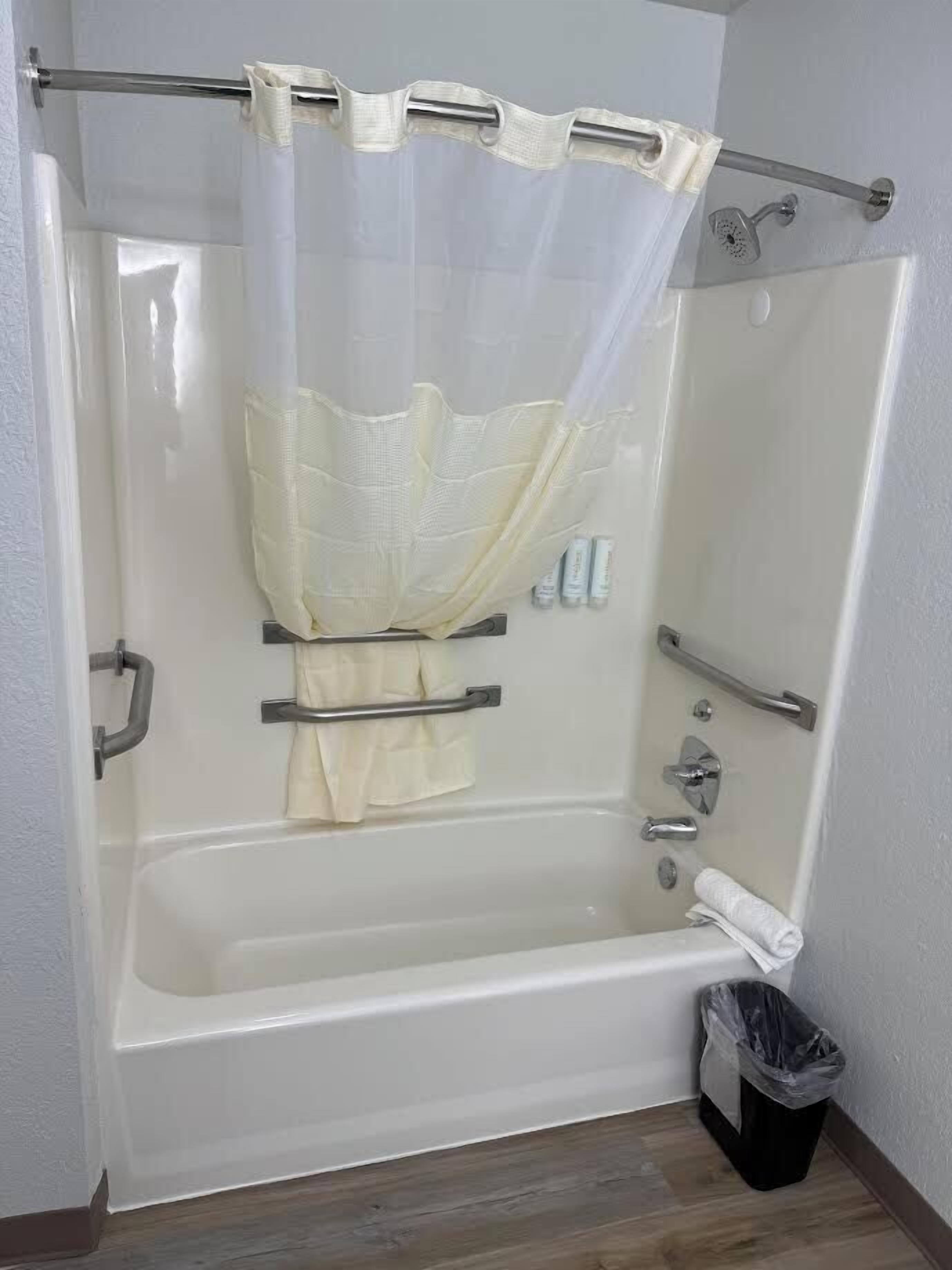 A walk-in shower with a glass door, a towel rack, a handheld showerhead, and a trash bin.