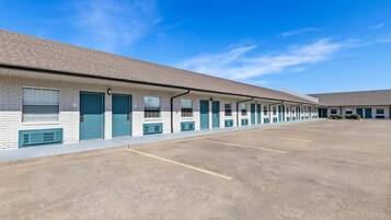 A row of motel rooms with individual doors and windows, a parking lot, and a clear blue sky.